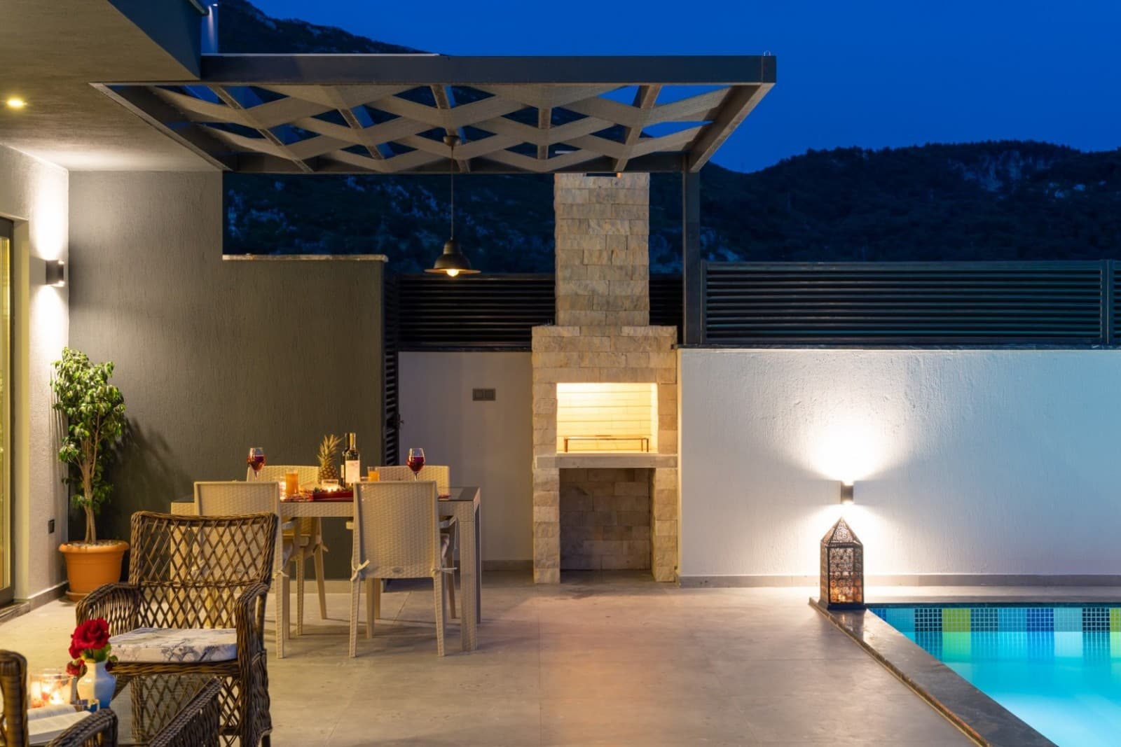 Havuz başındaki verandada yemek masası, barbekü ve rattan oturma grubu.