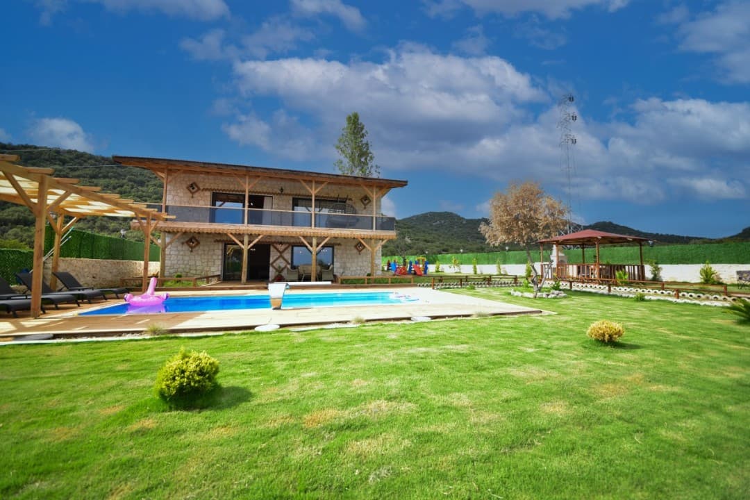 Geniş çimli bahçesi, yüzme havuzu ve çardağı olan iki katlı taş villa.