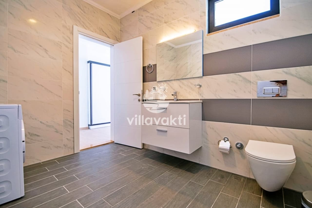 Mermer görünümlü seramik banyoda klozet ve beyaz dolaplı lavabo bulunuyor.