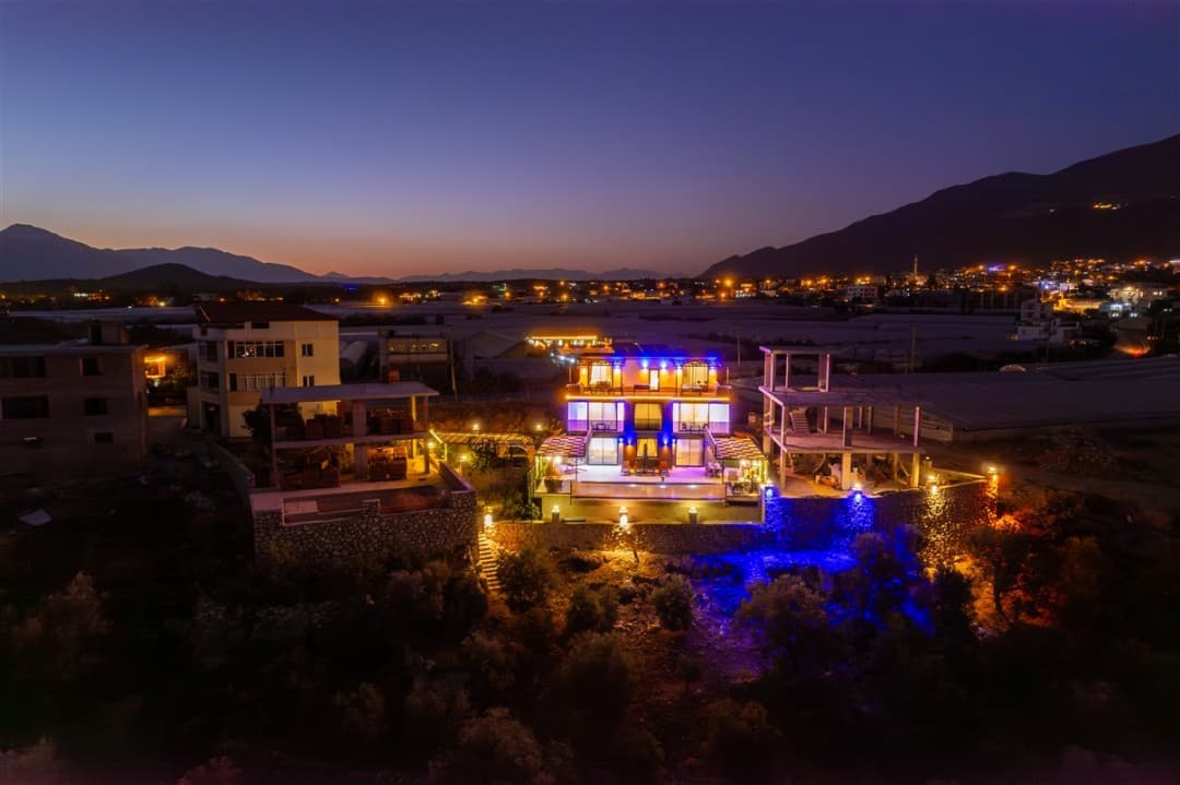 Gece vakti ışıklandırılmış, havuzlu ve teraslı villanın havadan görünümü.