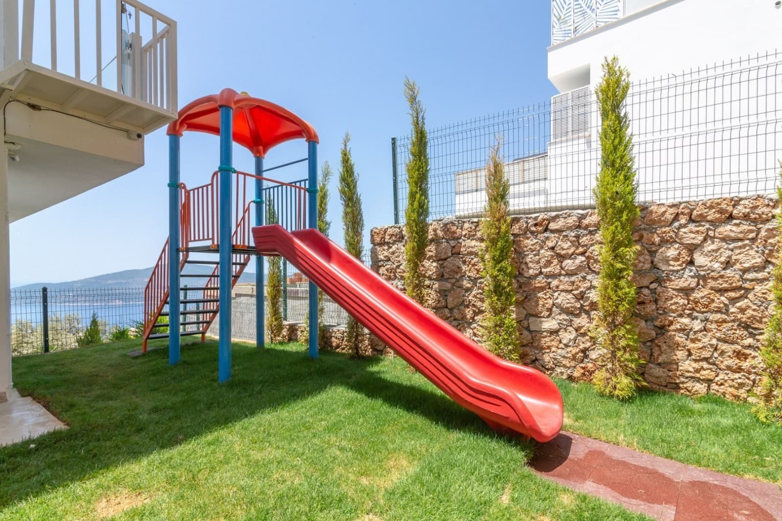 Yeşillikler içinde kırmızı kaydıraklı çocuk oyun parkı.