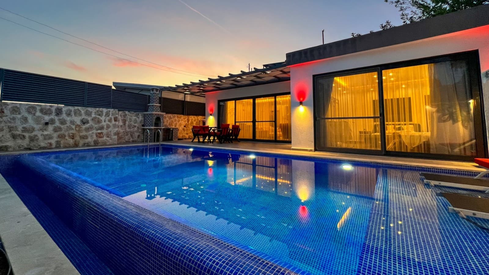 Akşam ışıklandırmalı havuz kenarı ve arkasında villa dış cephesi.