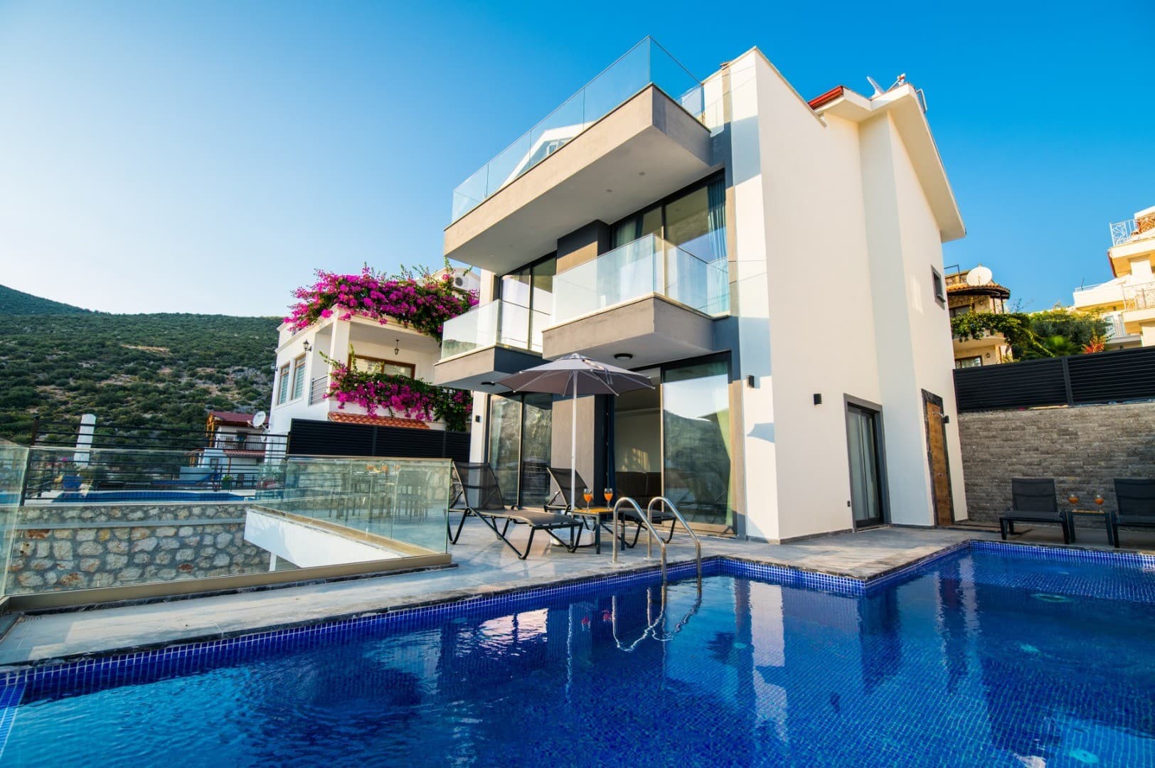 Mavi yüzme havuzlu ve şezlonglu modern iki katlı villa.