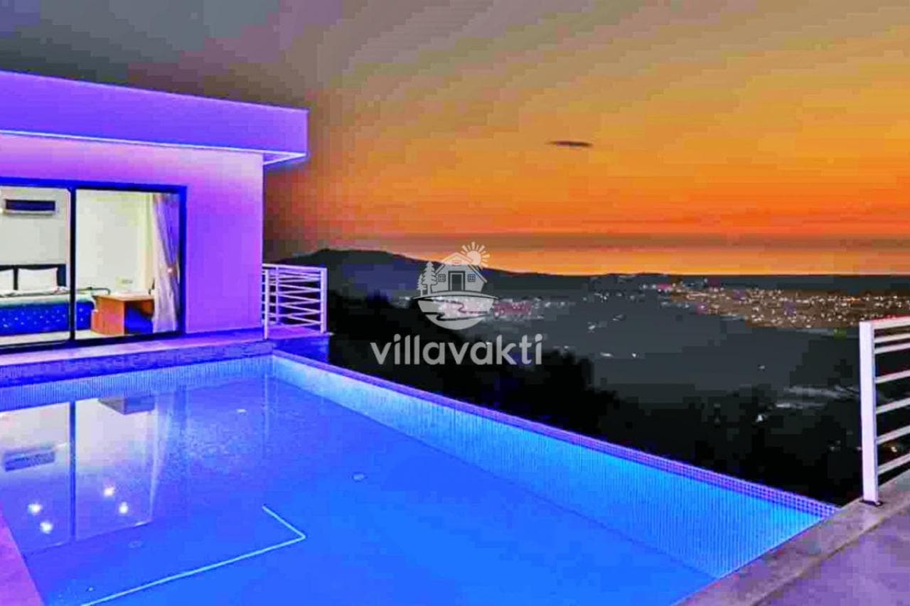 Gün batımında aydınlatmalı havuz kenarından dağ ve şehir manzarası.