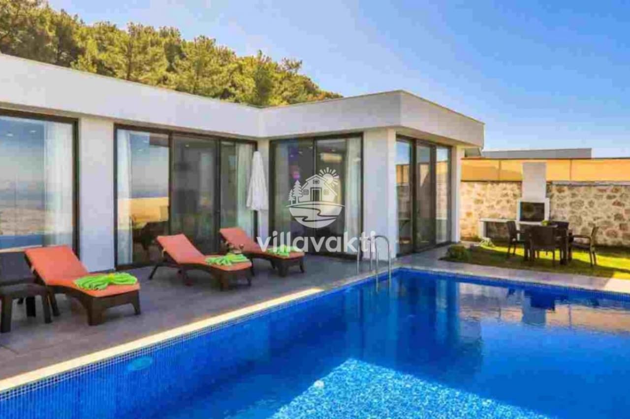 Havuz kenarında şezlonglar ve arka planda orman manzaralı villa cephesi.