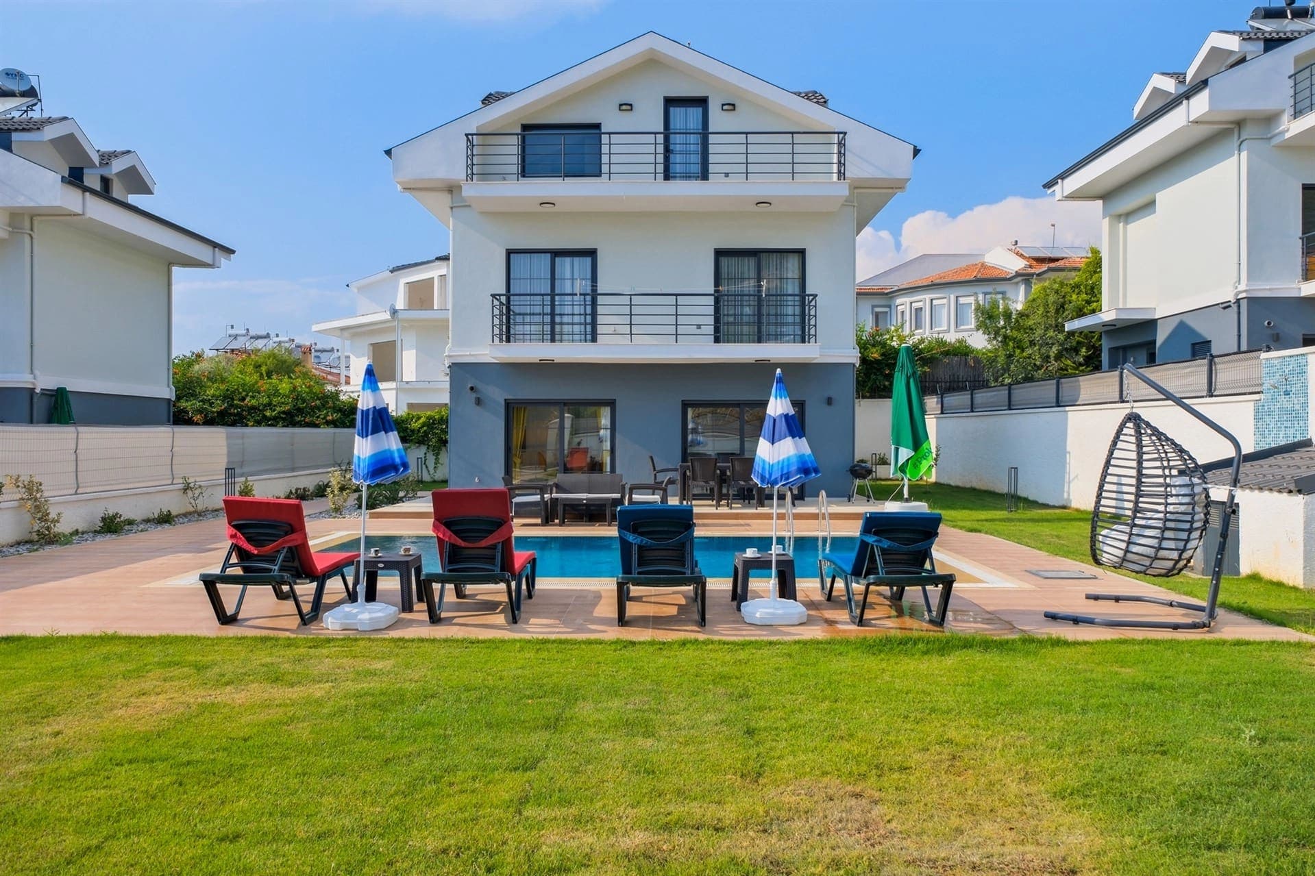 Çim bahçesi ve havuzu olan iki katlı modern villanın dış görünümü.