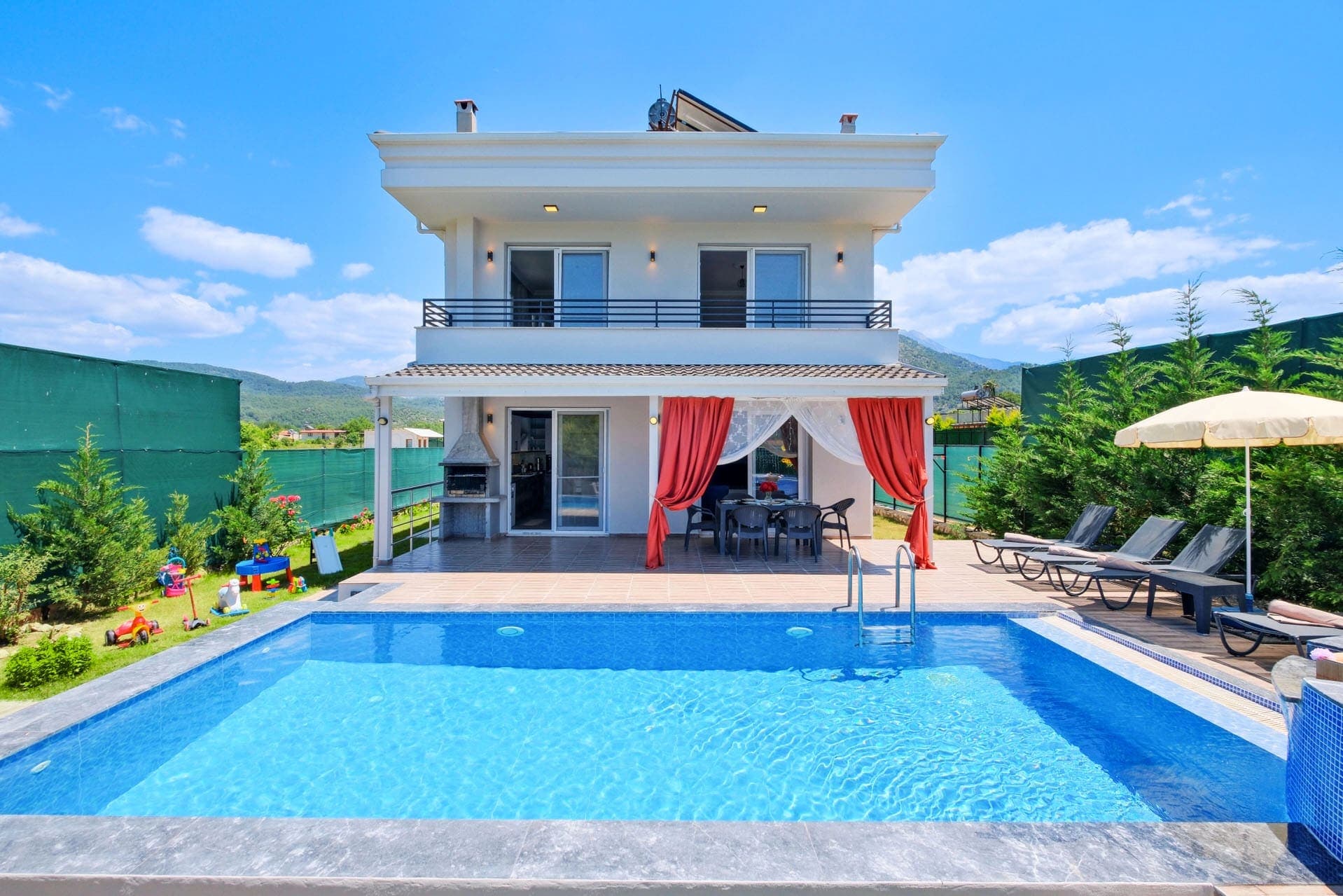 Bahçesinde havuz ve şezlonglar bulunan iki katlı beyaz villa dış cephesi.