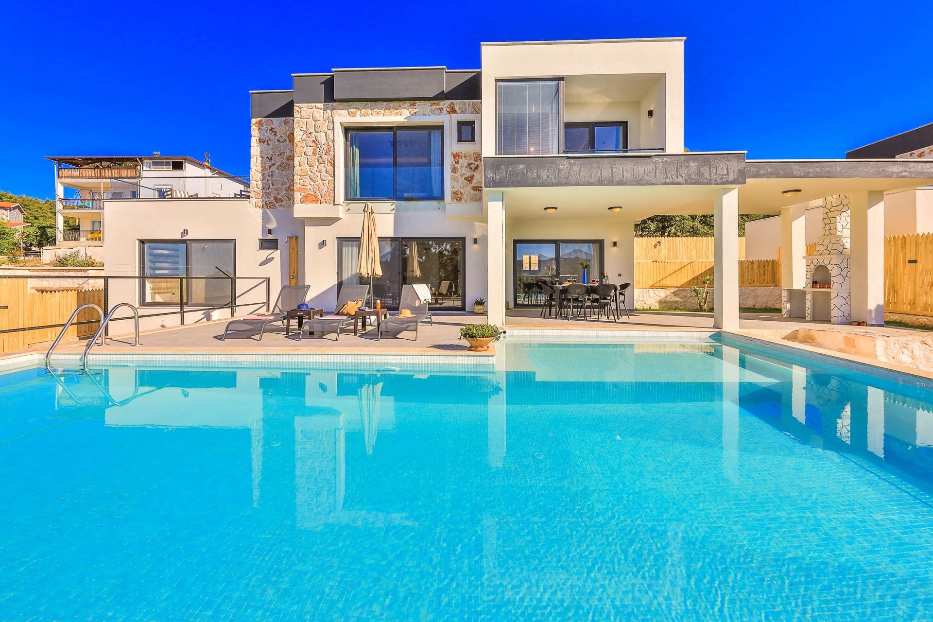 Geniş yüzme havuzu ve taş detaylı modern villanın dış cephesi.