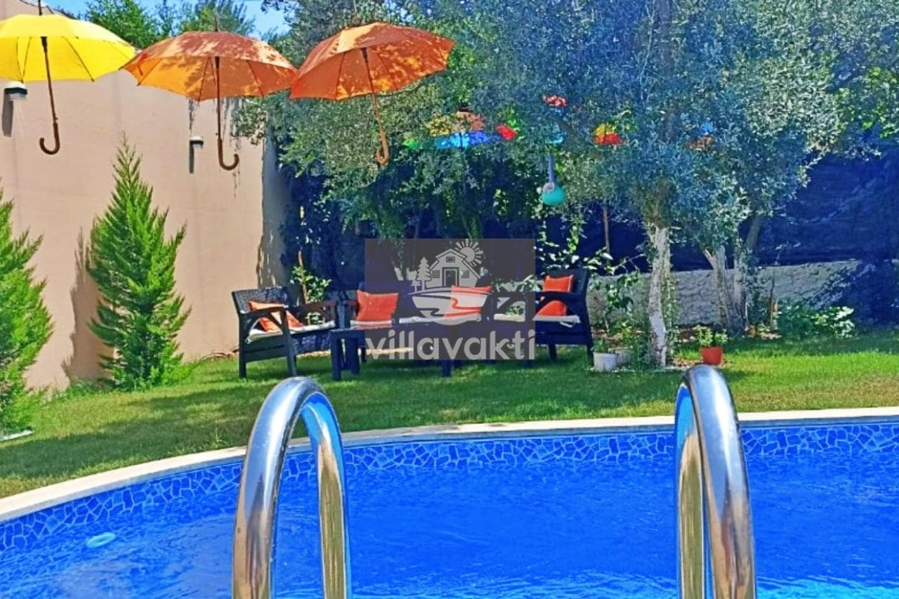 Ağaçlar altındaki havuz kenarında şemsiyeler ve oturma grubu bulunur.