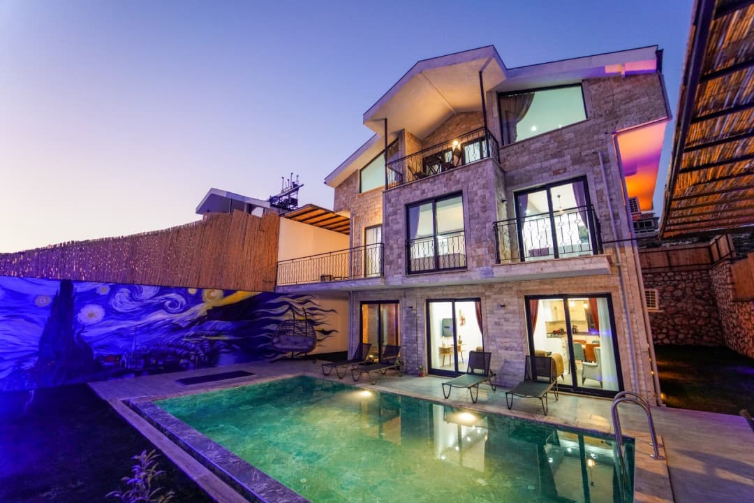 Alacakaranlıkta aydınlatılmış havuz ve iki katlı taş villa.