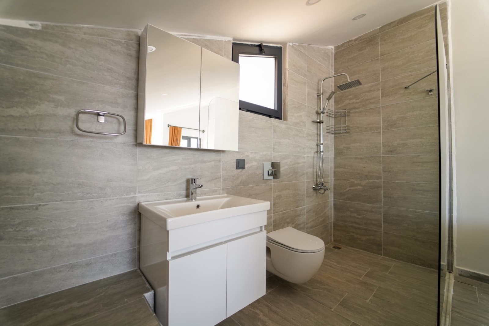 Gri tonlarında seramik kaplı banyoda duş kabini ve beyaz lavabo.