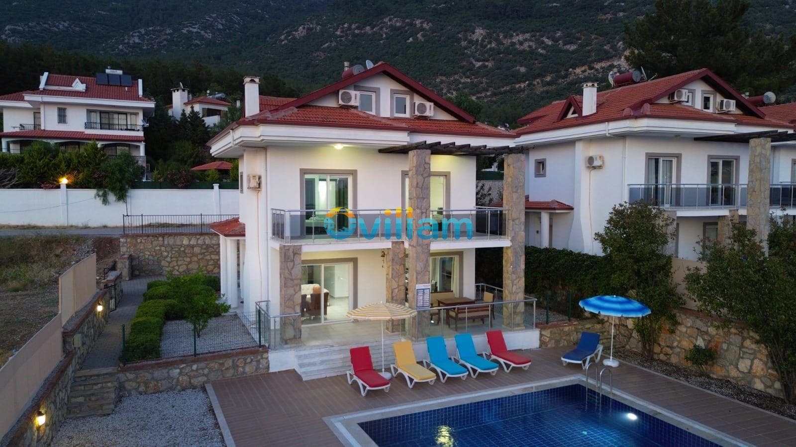 Akşam ışıklarında havuzu ve şezlongları görünen iki katlı villa.