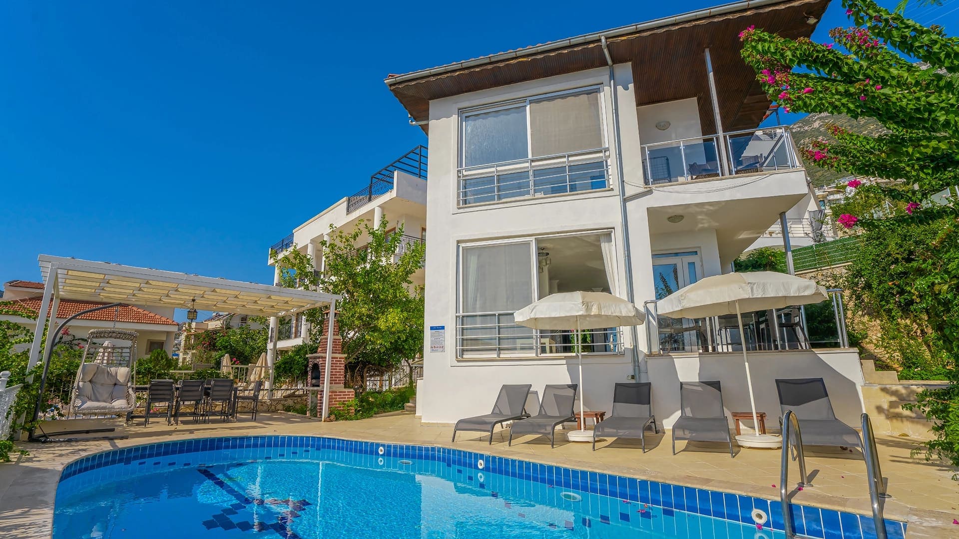 Önünde havuz, şezlonglar ve veranda bulunan beyaz dış cepheli villa.