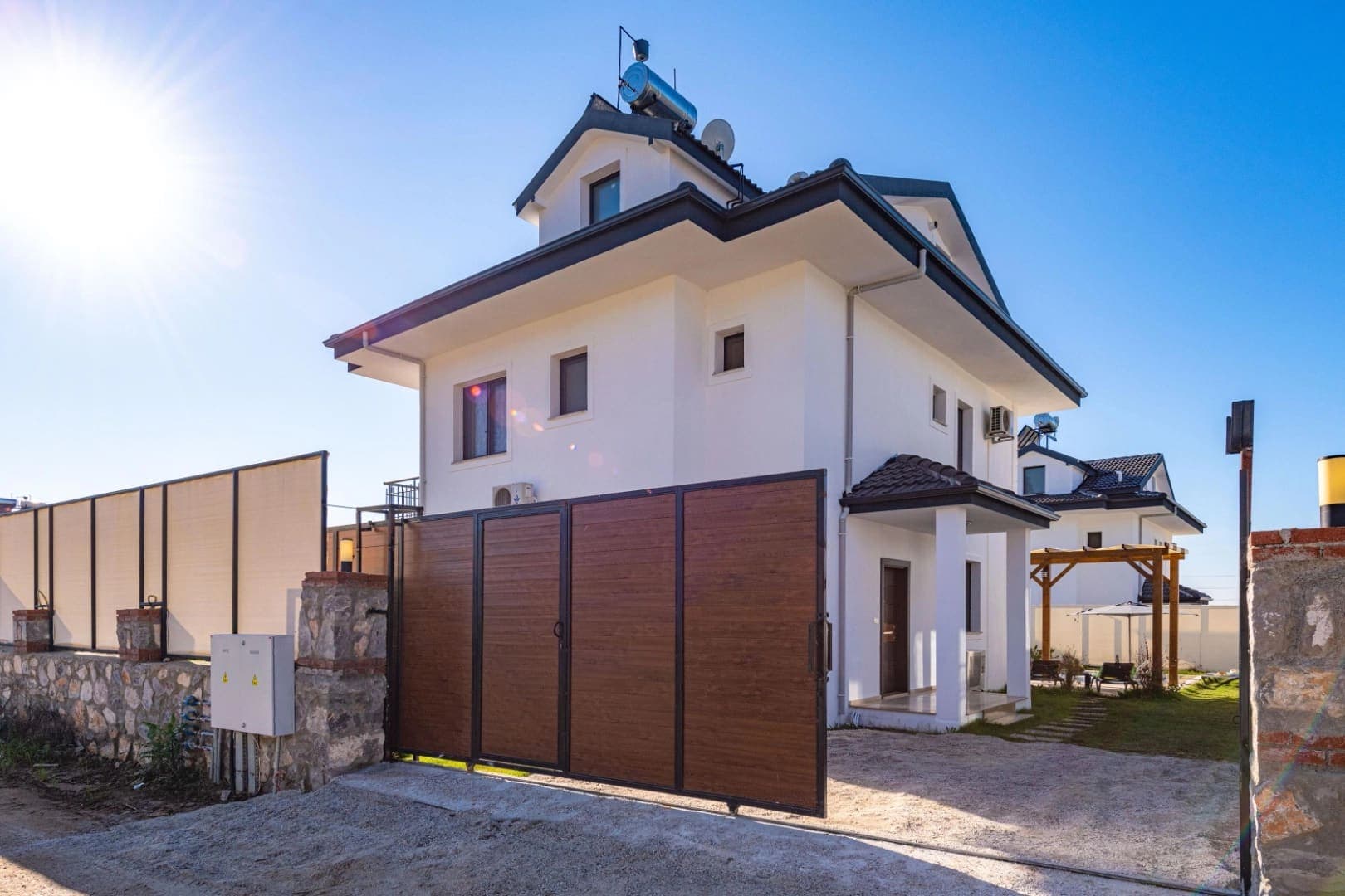 Ahşap sürgülü kapısı ve bahçe duvarı olan iki katlı beyaz villa.