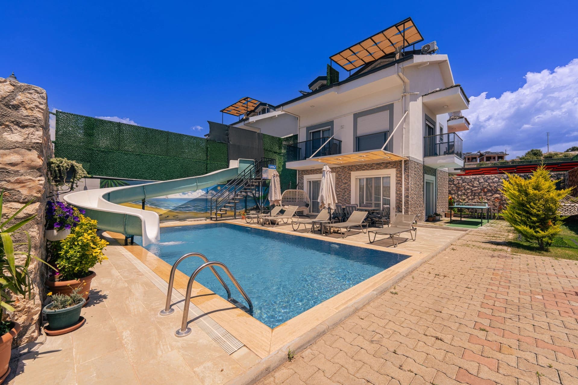 Kaydıraklı havuzu ve şezlongları olan, taş kaplamalı müstakil villa dış cephesi.