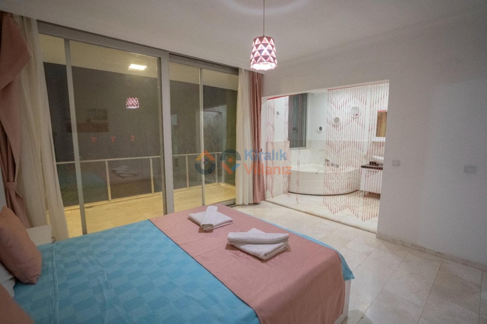 Çift kişilik yatak ve açık plan jakuzili banyo alanı.