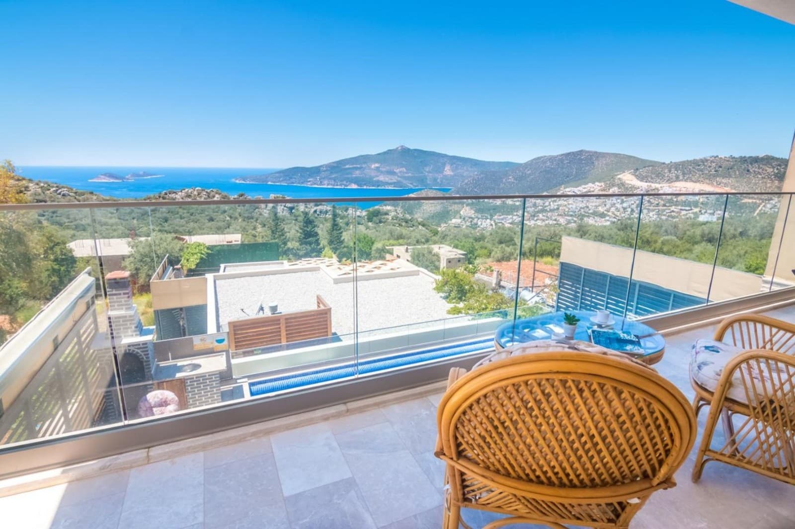Cam balkondan deniz ve dağ manzarası görünen, hasır sandalyeli balkon.