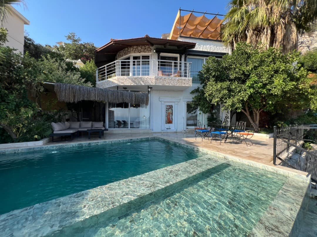 Önünde havuzu ve oturma grubu olan, ağaçlarla çevrili iki katlı beyaz villa.