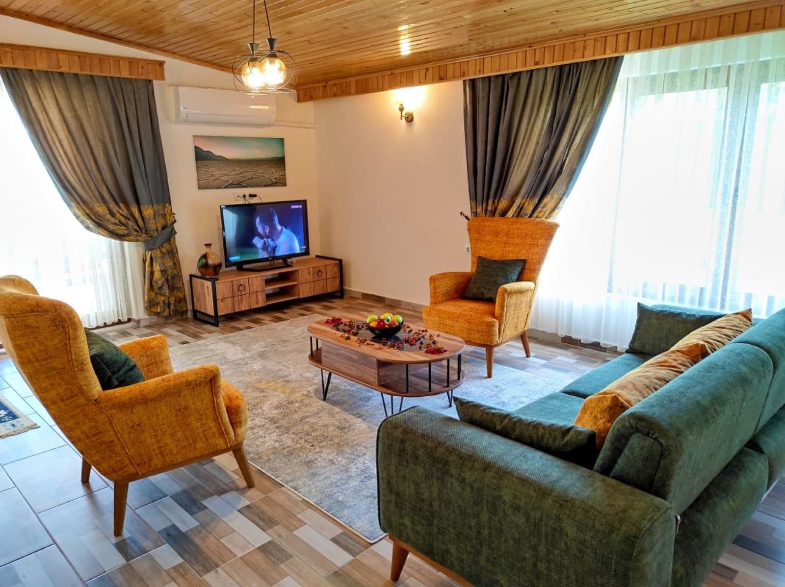 Oturma odasında yeşil kanepe, sarı berjerler ve televizyon.
