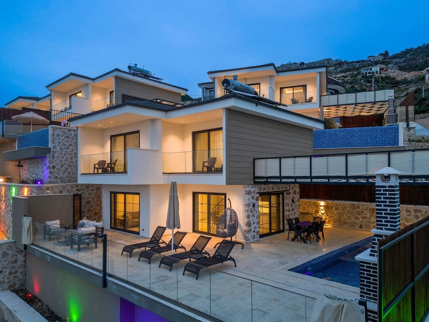 Geniş teraslı, havuzlu ve akşam ışıklandırmalı modern villanın dış görünümü.
