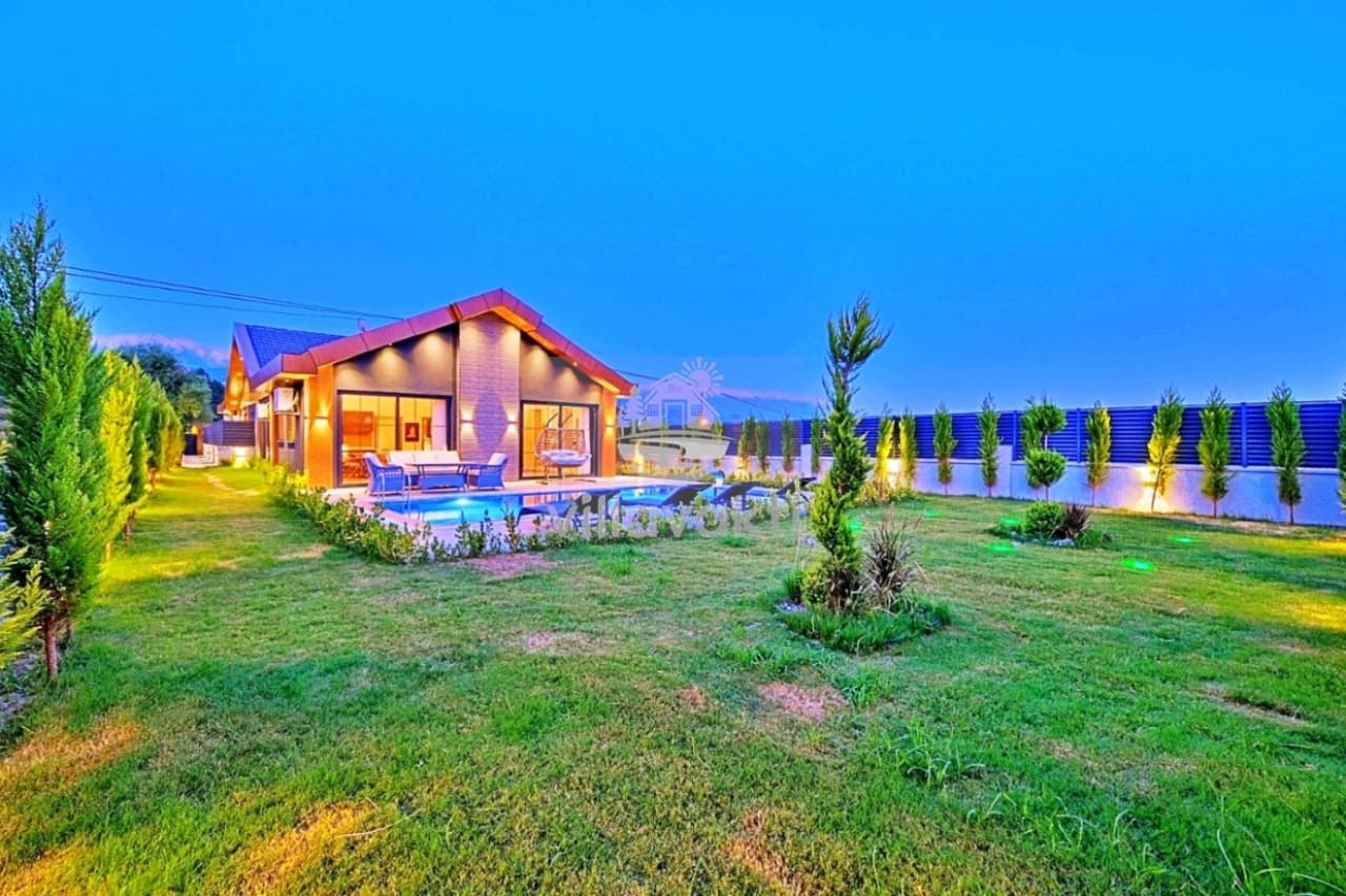 Bahçesinde havuz bulunan, akşam aydınlatmalı tek katlı villanın geniş çim alanı.