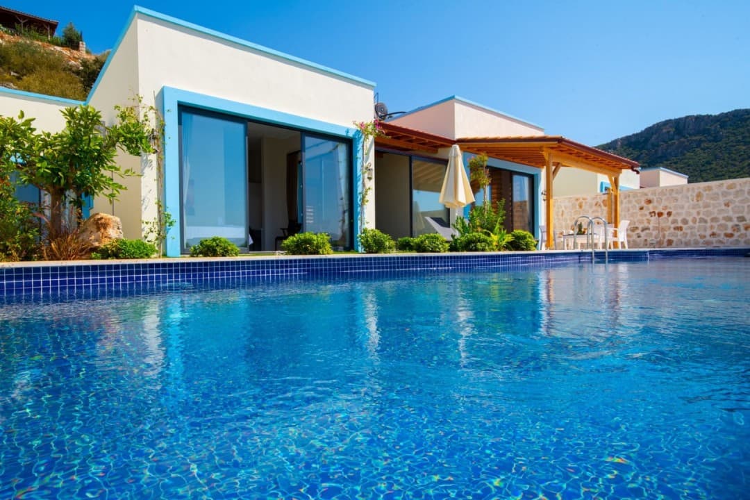 Mavi detaylı modern villanın önünde yer alan açık hava yüzme havuzu ve güneşli bir gökyüzü.