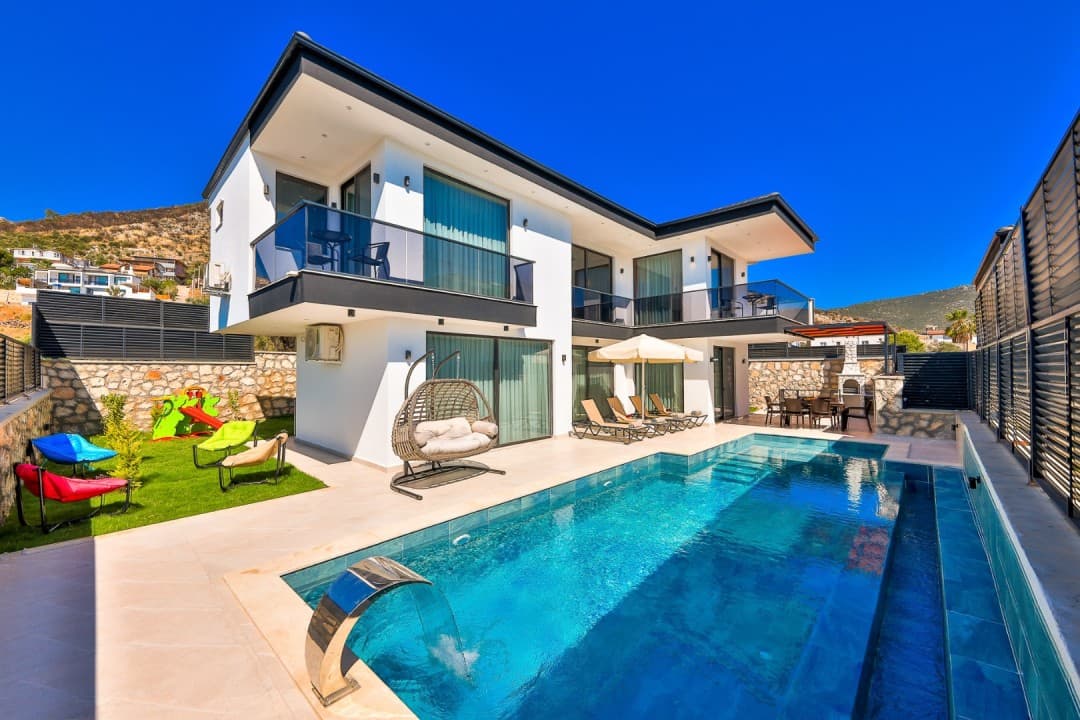 Önünde havuzu ve bahçesinde oyun alanı olan iki katlı modern villa.