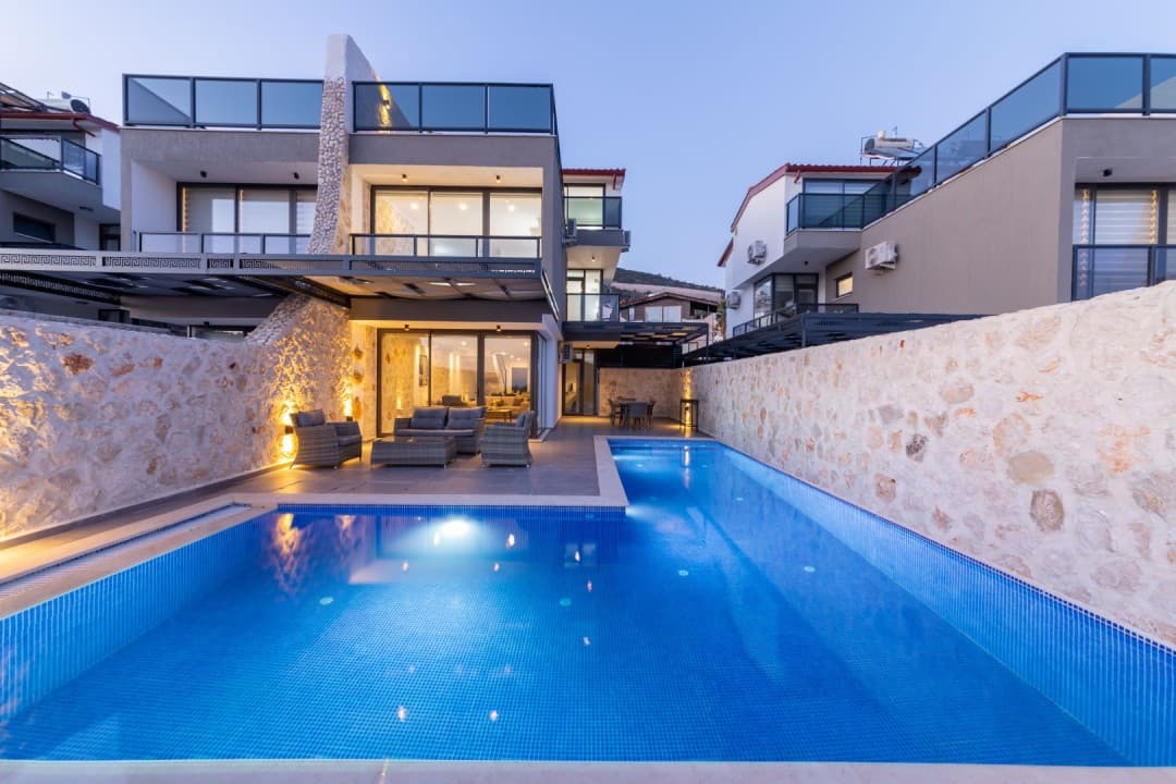 Akşam vakti aydınlatılmış, taş duvarlı ve özel yüzme havuzlu modern villa dış cephesi.