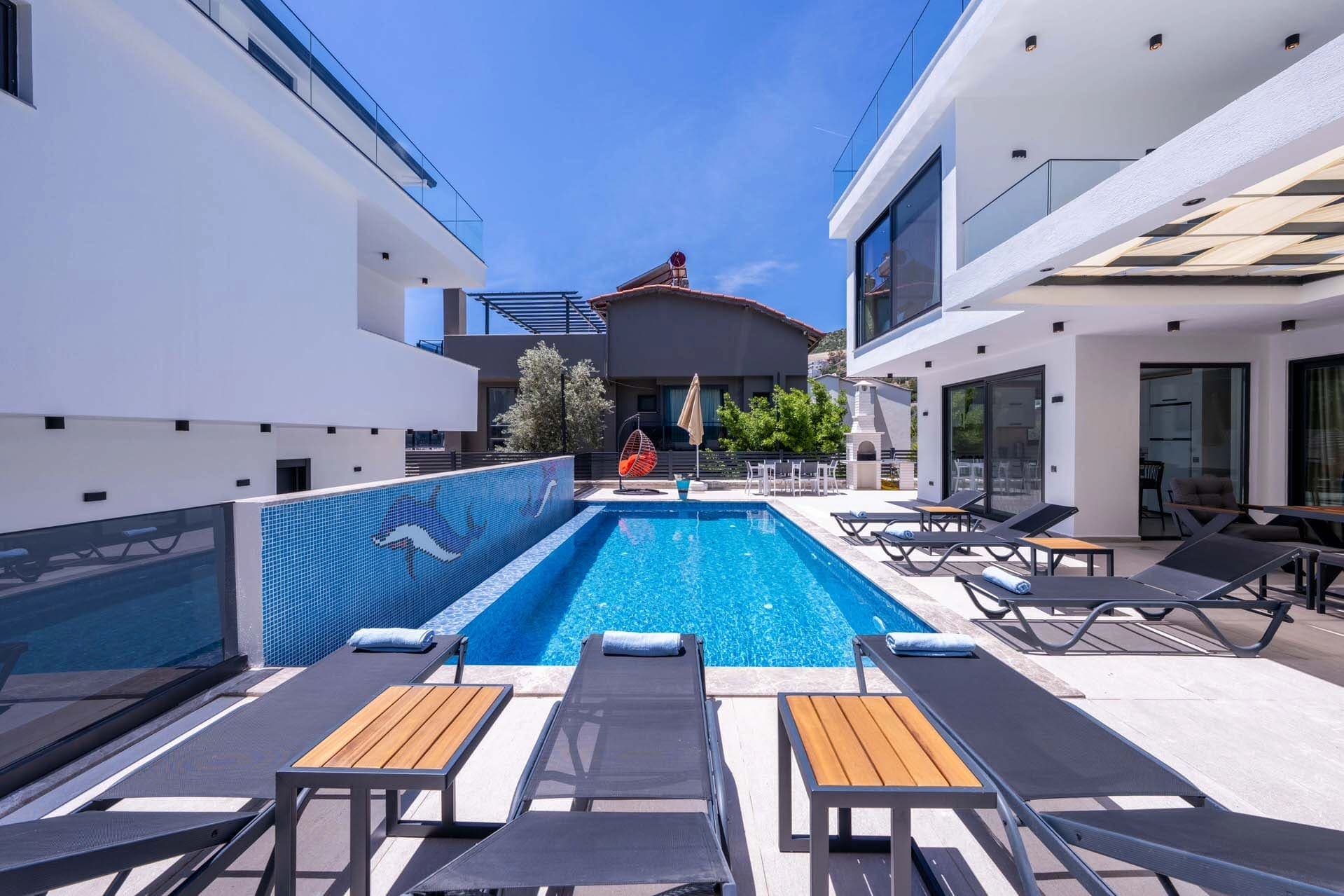 Şezlonglar ve havuz kenarında şemsiyeler bulunan modern villa avlusu.