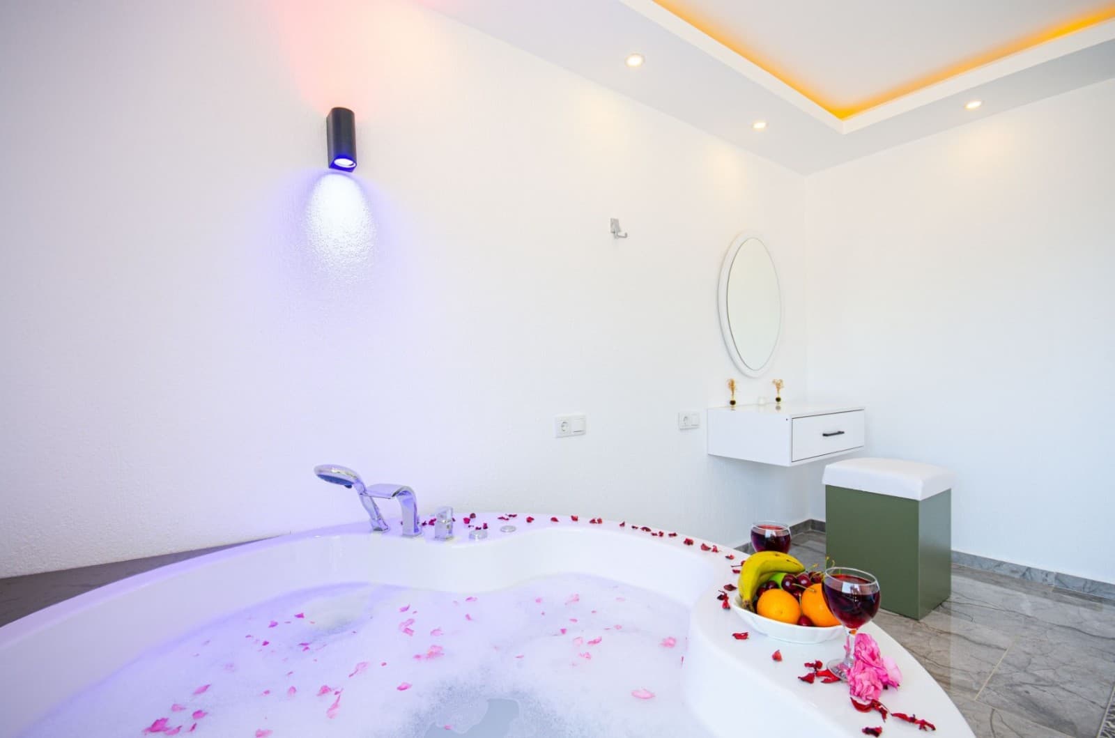 Gül yaprakları ve meyve tabağıyla süslenmiş yuvarlak jakuzi banyo.