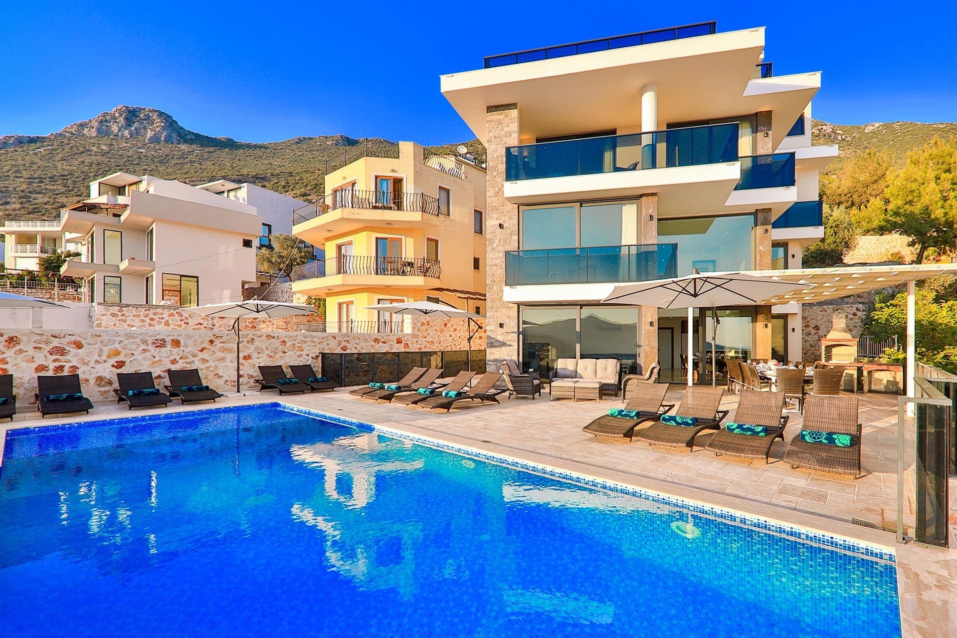 Geniş yüzme havuzu ve şezlongları bulunan çok katlı modern villa.