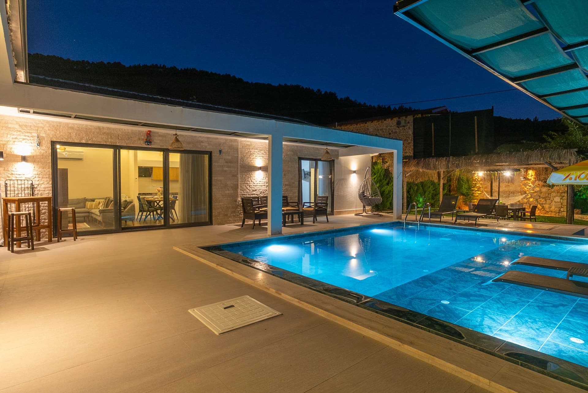 Aydınlatmalı yüzme havuzu ve geniş teraslı modern villanın gece görünümü.