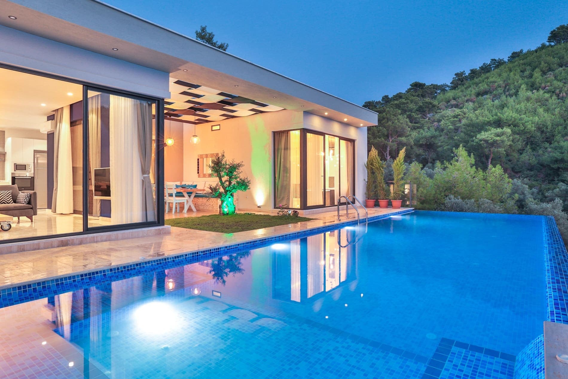 Akşam ışıklandırmalı havuz ve modern villanın dış cephesi.