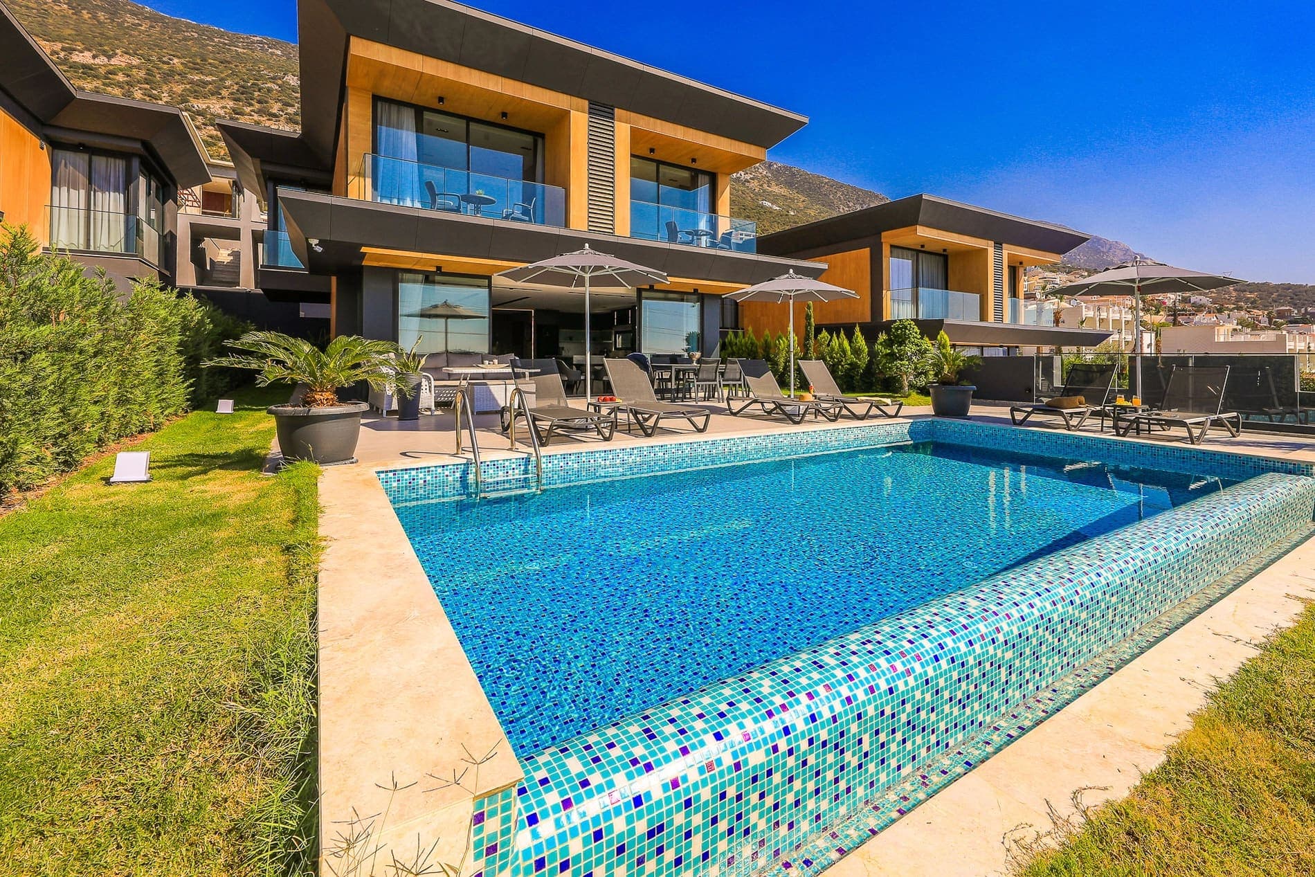 Havuz kenarında şezlonglar ve şemsiyeler bulunan modern villanın dış cephesi.