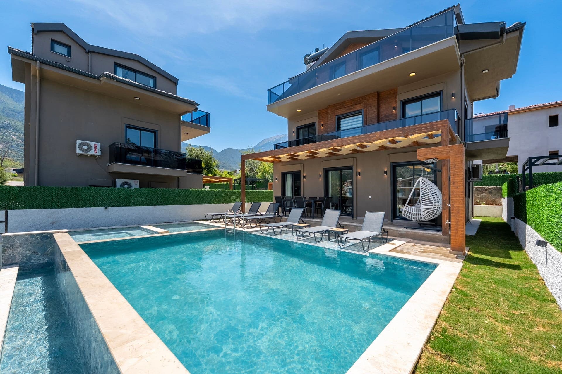 Geniş havuzlu ve şezlonglu modern villanın dış cephesi ve bahçesi.