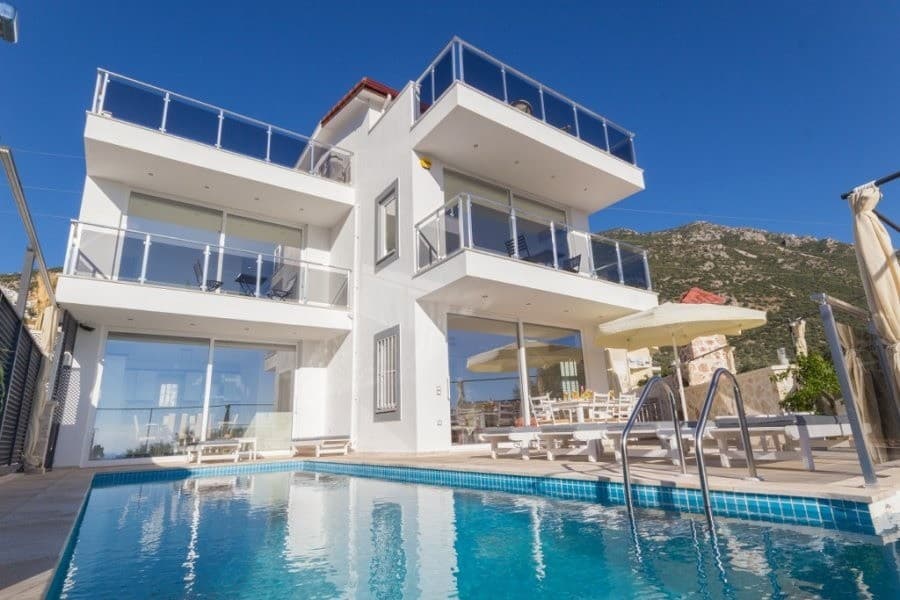 Mavi gökyüzü altında yüzme havuzlu beyaz dış cepheli çok katlı villa.