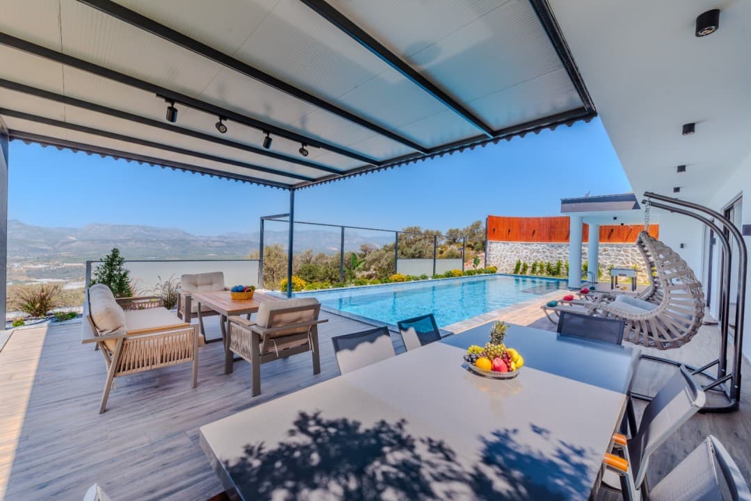 Veranda kısmında yemek masası, oturma grubu, salıncak ve açık havuz bulunan manzaralı villa terası.
