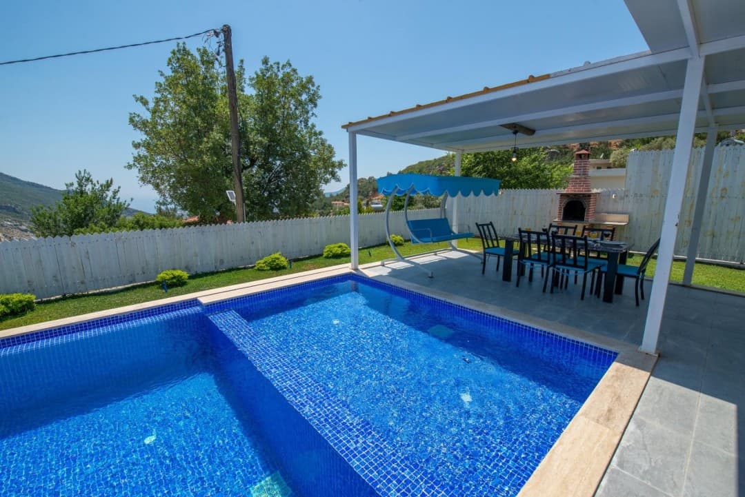 Açık havada havuz kenarında mavi salıncak, yemek masası ve barbekü alanı.
