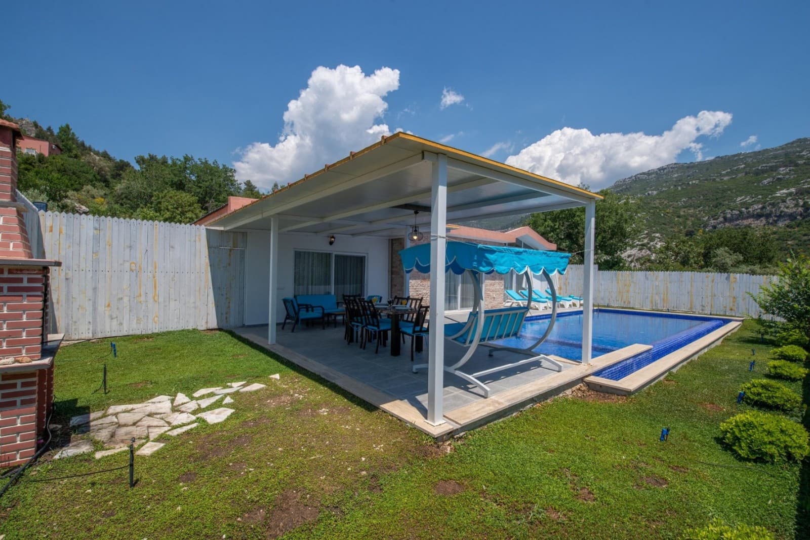 Çim bahçe içerisinde havuz, veranda altında oturma grubu ve mavi salıncak.