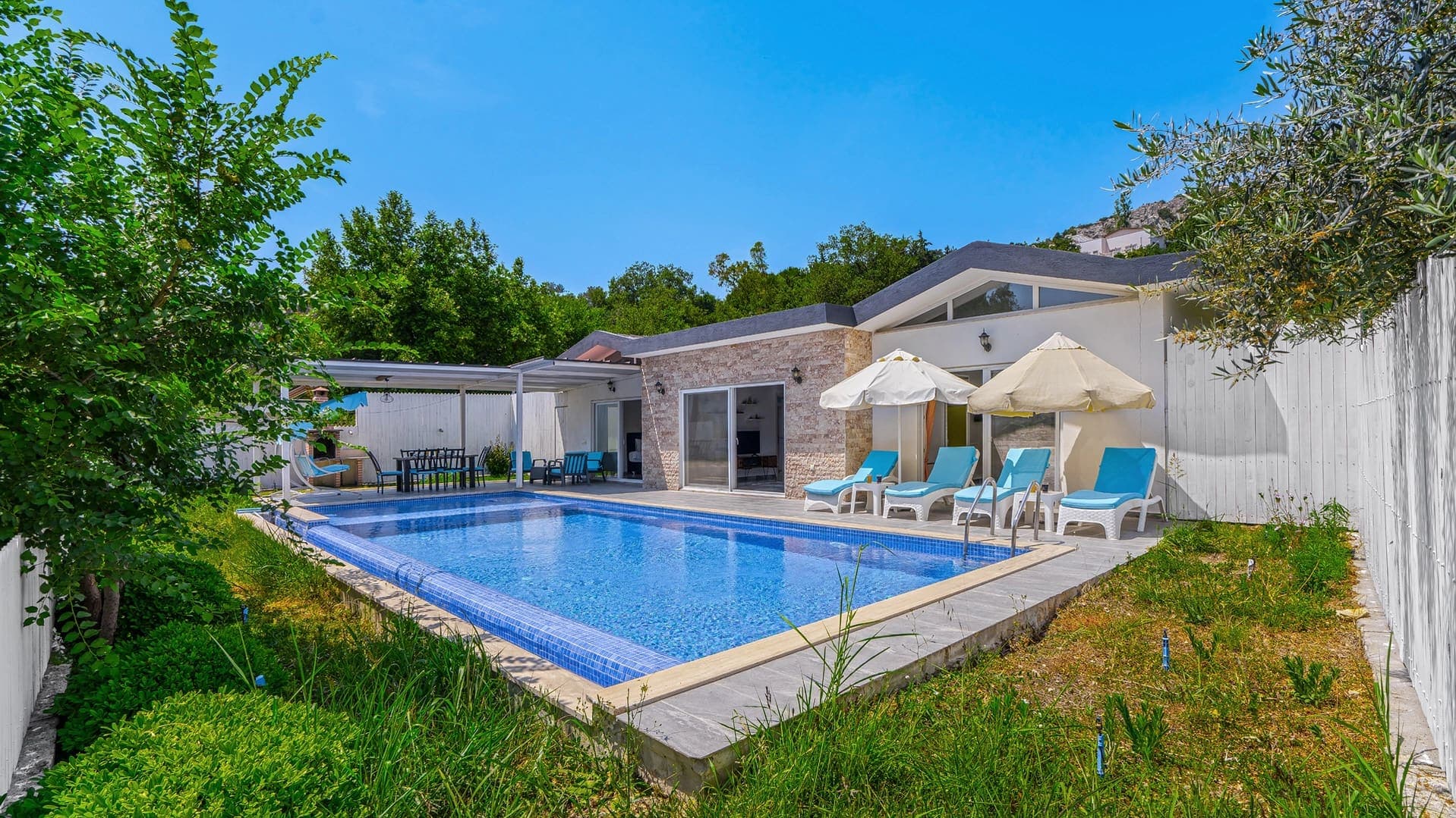 Bahçe içinde, şezlonglu havuzu bulunan tek katlı modern villa.