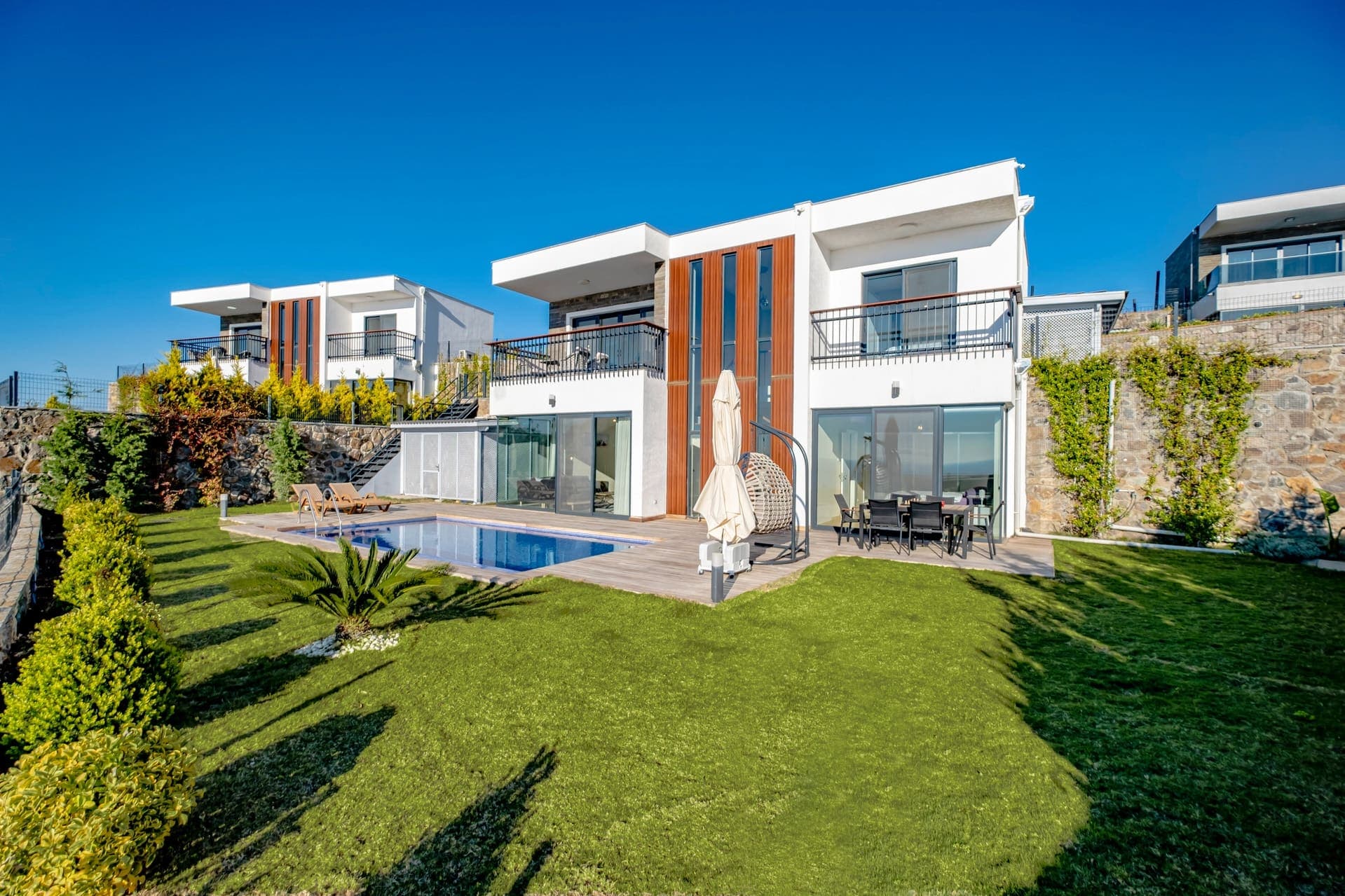 Önünde havuz ve çim alan bulunan iki katlı beyaz villa.