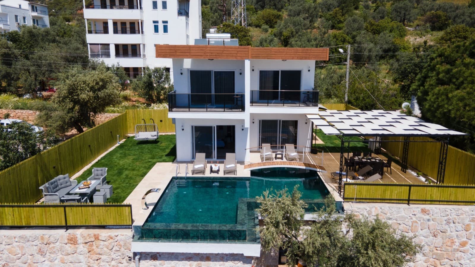 İki katlı modern villanın önünde koyu renkli havuz ve yemek masası bulunuyor.
