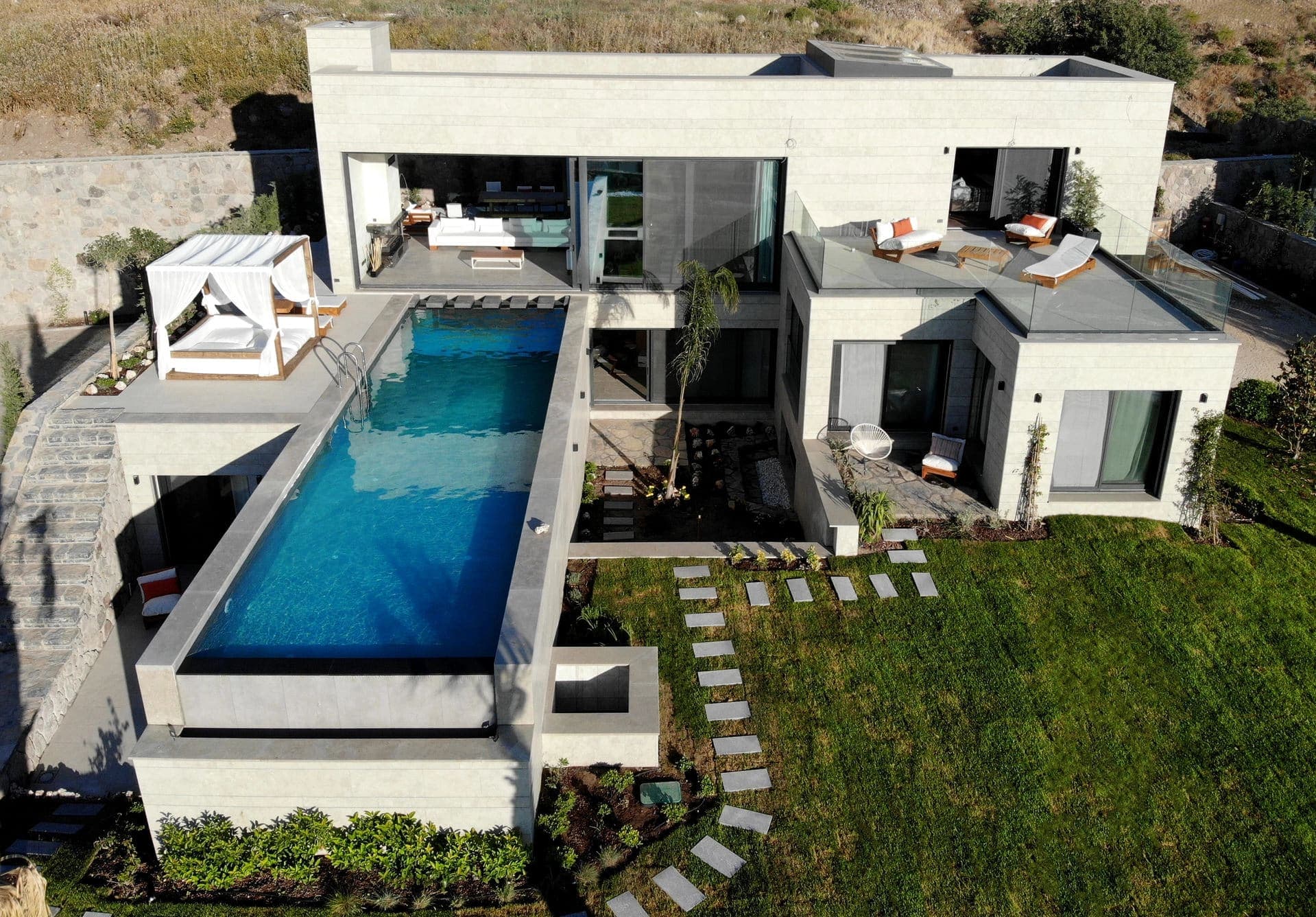 Havuz kenarında şezlonglar ve oturma grubu bulunan modern villa cephesi.