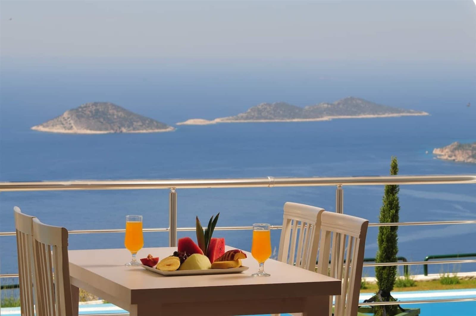 Balkonda meyve tabağı ve bardaklar bulunan masanın arkasında deniz ve adalar.
