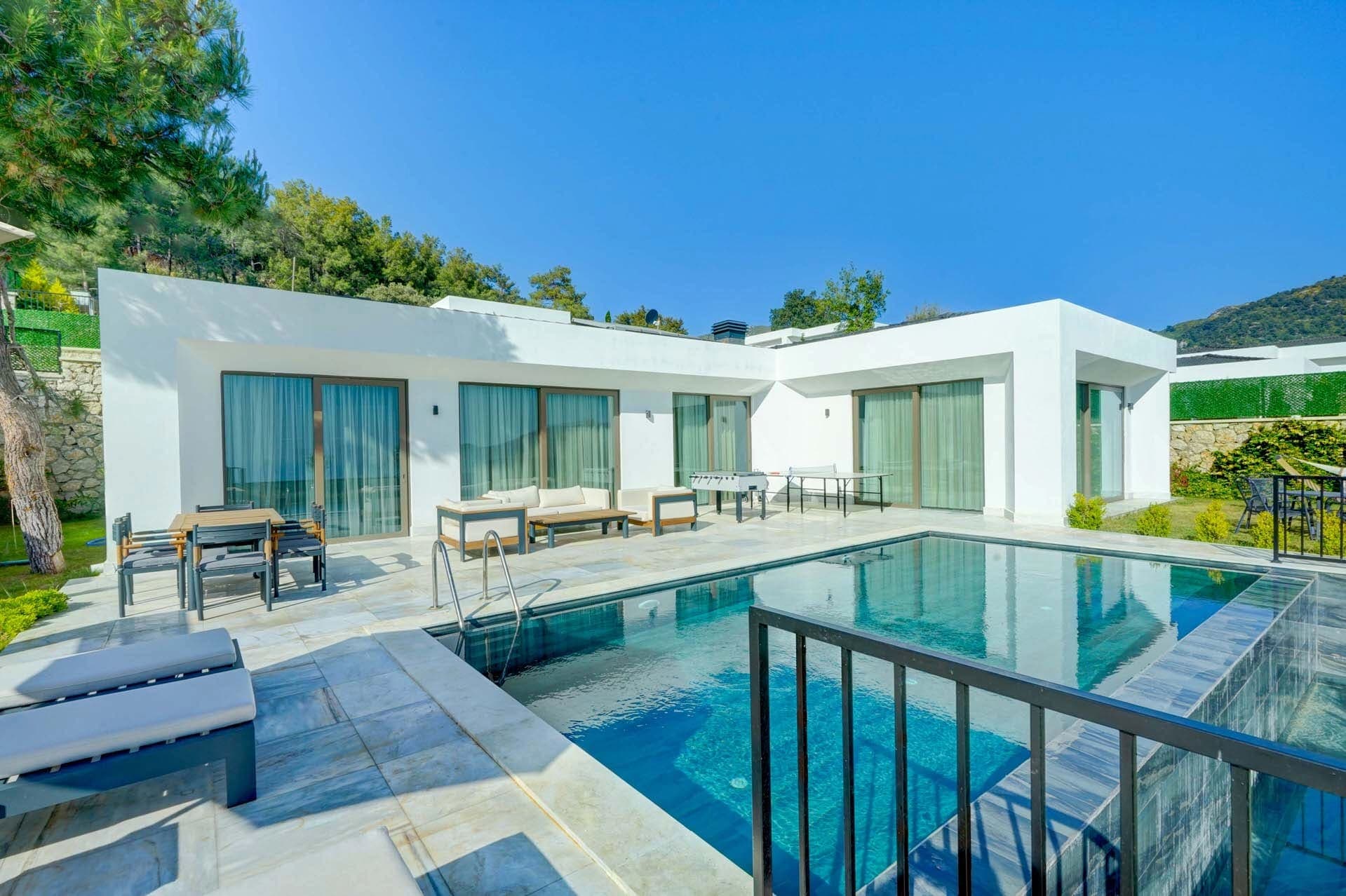 Önünde havuz ve şezlonglar yer alan beyaz dış cepheli villa.