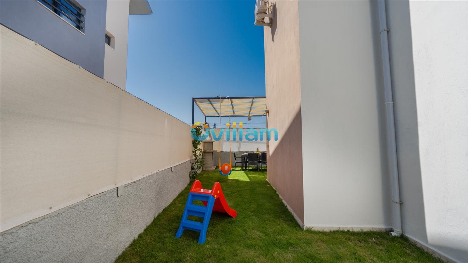 Bahçesinde çocuk kaydırağı ve salıncak bulunan villa kenarı.