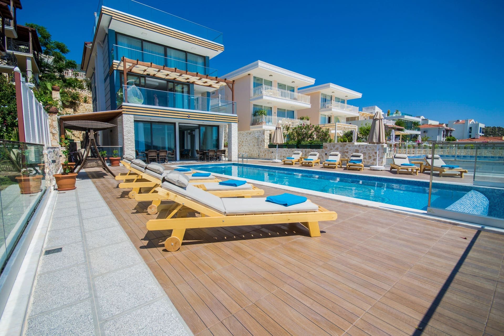 Güneşli günde havuz kenarında şezlonglar bulunan modern villa.