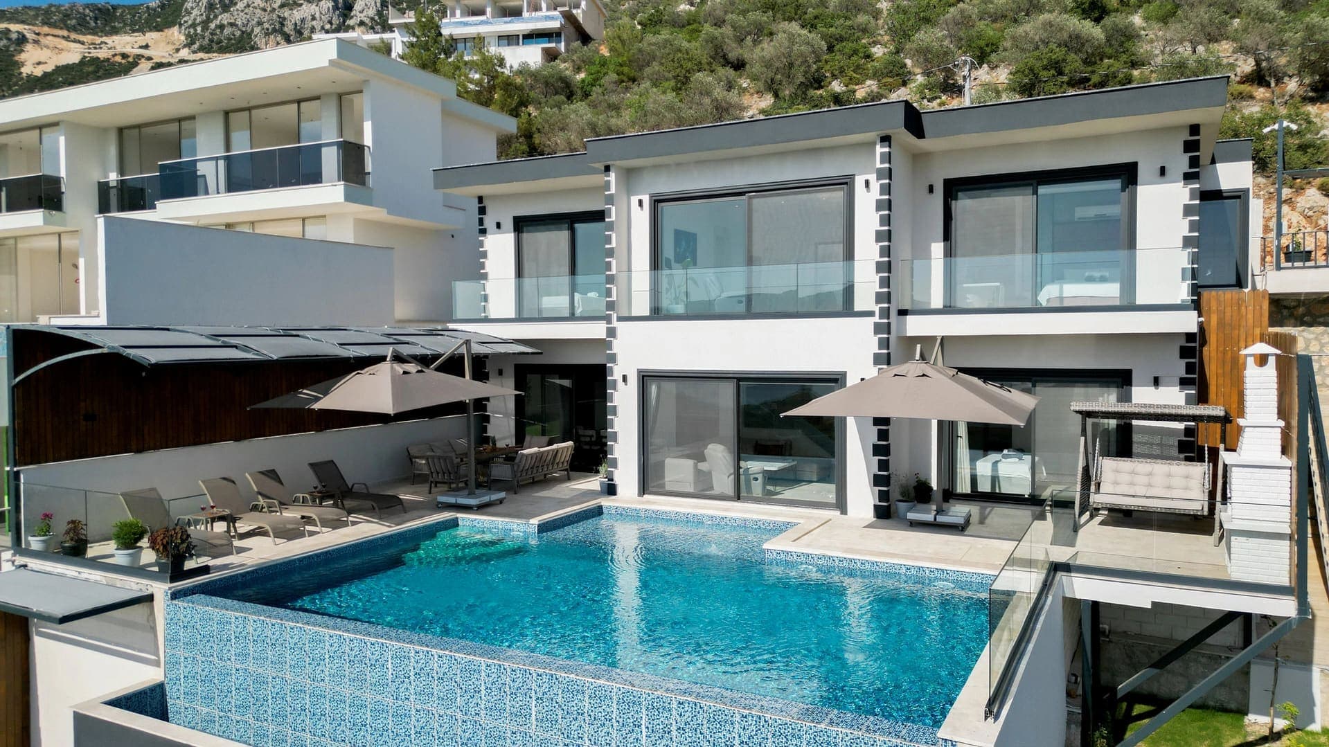 Havuz başında şezlonglar ve şemsiyeler bulunan modern beyaz villa.