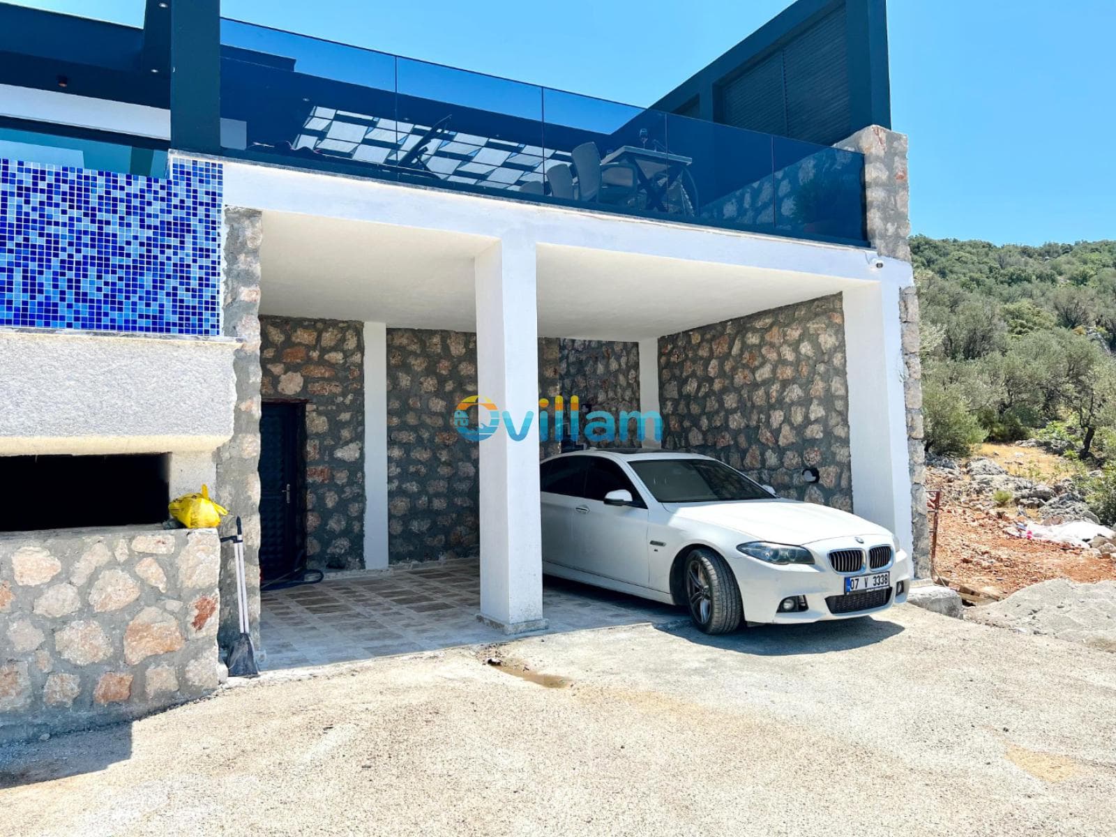Taş duvarlı villanın üstü kapalı otoparkında park etmiş beyaz bir otomobil.
