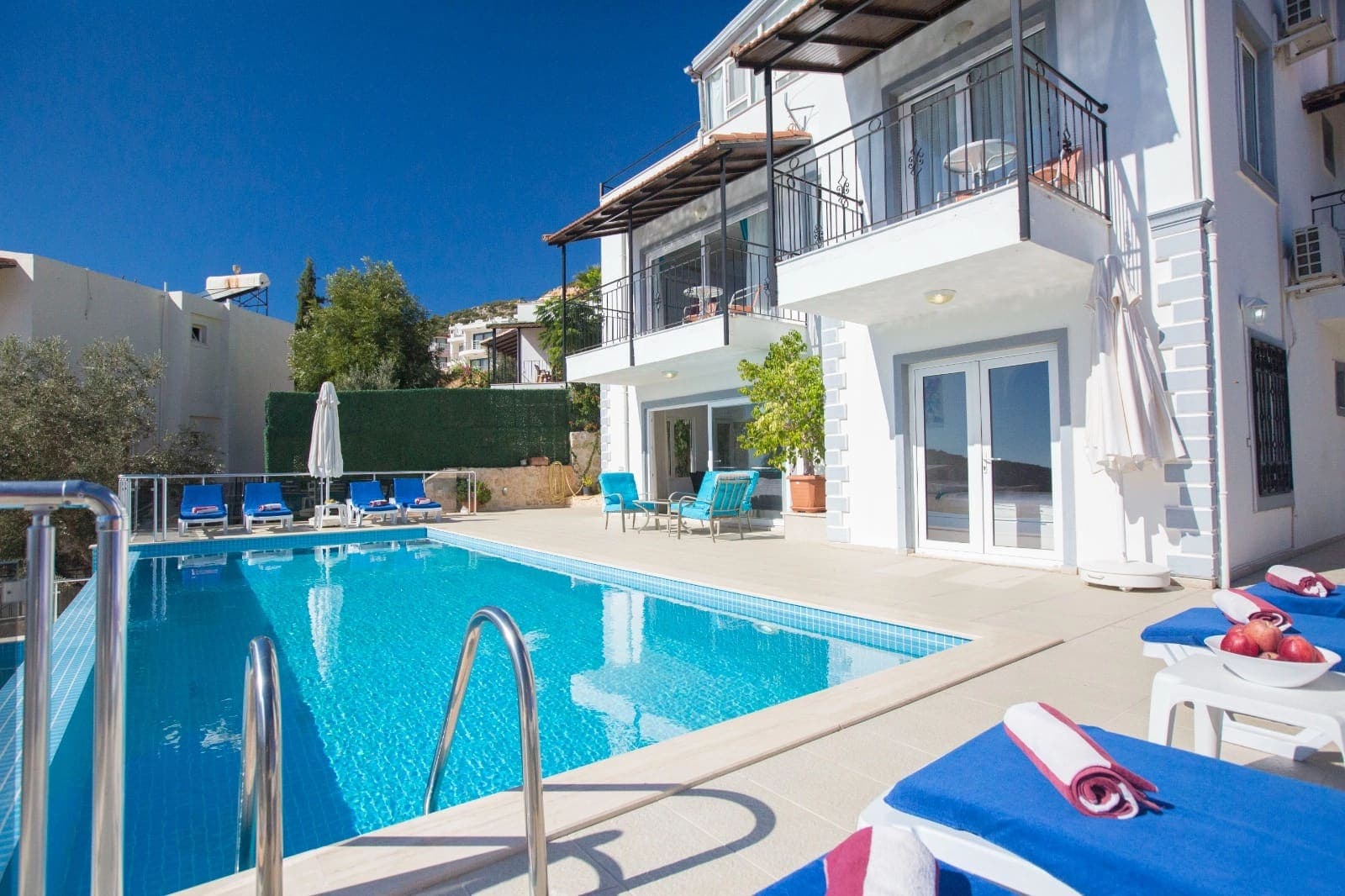 Önünde havuzu ve şezlongları olan, beyaz cepheli iki katlı villa.